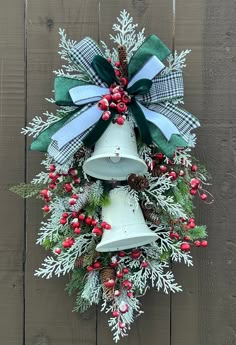 a christmas wreath hanging on the side of a wooden fence with bells and evergreens