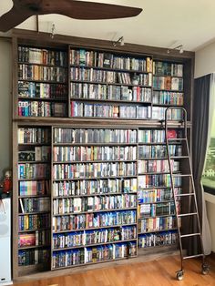 a book shelf filled with lots of books next to a ceiling fan in a living room