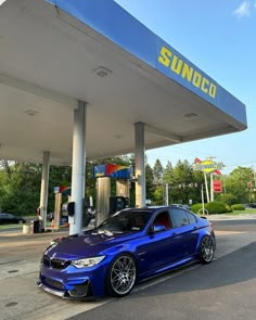 a blue bmw is parked in front of a sunoco gas station