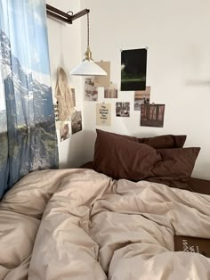 an unmade bed with brown sheets and pictures on the wall next to it in front of a window