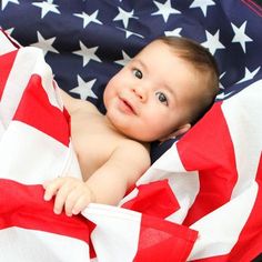 a baby wrapped in an american flag blanket looking up at the camera while laying on it's back