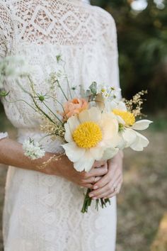 a woman in a white dress holding a bouquet of yellow and white flowers on her wedding day