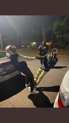 two people are dancing on the street in front of a car and another person is standing behind them