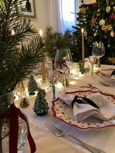 a table set for christmas dinner with silverware, candles and plates in front of a christmas tree