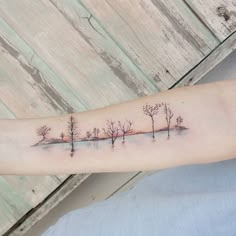 a person with a tattoo on their arm that has trees in the snow and water