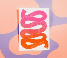 an orange and pink snake on a white card against a multicolored background with the letter s