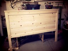 a wooden bed frame in a garage with a bicycle hanging on the wall behind it