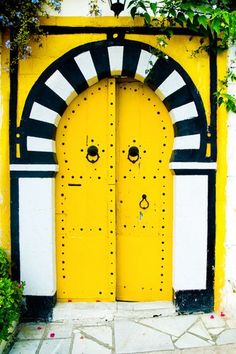 a yellow door with two black and white designs on it's sides in front of a building