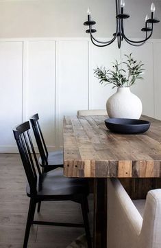 a dining room table with a vase on top of it next to two chairs and a chandelier