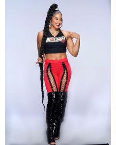 a woman in black top and red pants with braids on her head standing next to a white wall