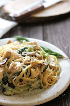 pasta with chicken, broccoli and mushrooms on a white plate sitting on a wooden table