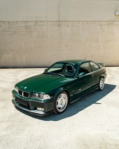 a green sports car parked in front of a building with concrete walls and cement flooring