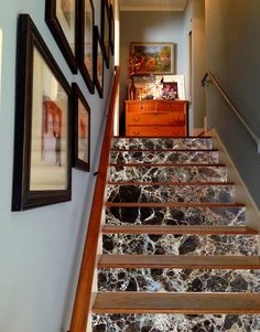 the stairs are lined with pictures and framed on the wall above them, along with an antique chest of drawers