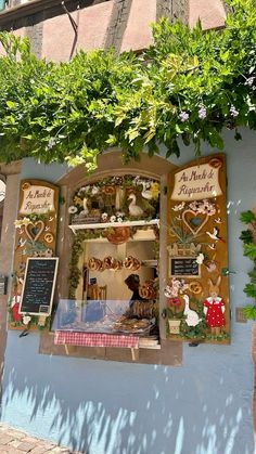 a store front with an assortment of items on display in the window and below it is a tree