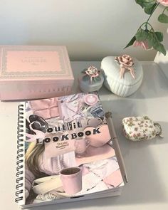 a pink book sitting on top of a white table next to a vase with flowers