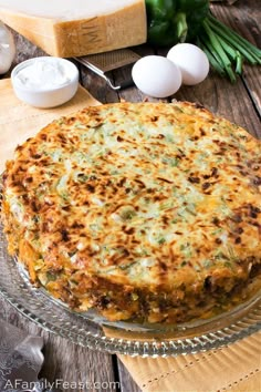 a cheesy casserole on a glass platter with eggs in the background