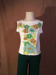 "1960s women's pullover sleeveless tee shirt label- Lane Colby Apparel boat neck white w/big orange/green flowers print cotton light weight jersey feel good vintage condition, light wear, a few tiny spots (see photos) sleeves look hemmed labeled L, see below measures, lying flat, shoulder-14 1/2\" chest-18\" to 21\" hem-18\" length-20\"" White Vintage Print T-shirt For Spring, Fitted Vintage Print T-shirt For Spring, Cotton Stretch T-shirt With Floral Print, Stretch Cotton T-shirt With Floral Print, Vintage Stretch T-shirt For Summer, Floral Print Stretch Cotton T-shirt, Green Vintage Print Short Sleeve Top, Vintage Stretch Tops With Graphic Print, White Vintage Stretch Top