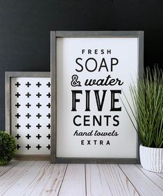 a white framed sign sitting on top of a wooden table next to a potted plant