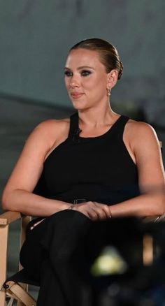 a woman sitting in a chair with her hand on her hip and looking at the camera