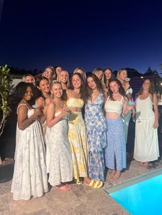 a group of women standing next to each other in front of a pool at night