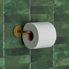 a roll of toilet paper is hanging on the wall next to a green tiled wall