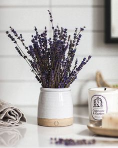 a white vase filled with purple flowers on top of a table next to a cup