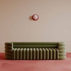 a green couch sitting on top of a pink floor next to a round wall clock