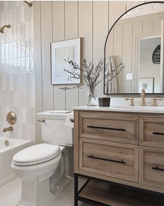 a white toilet sitting next to a bath tub in a bathroom under a mirror on top of a wooden cabinet