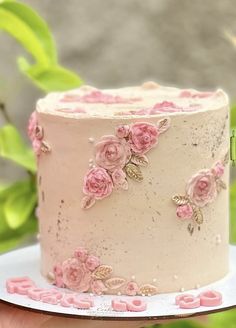 a hand holding a white cake with pink flowers on it and the top layer is covered in frosting