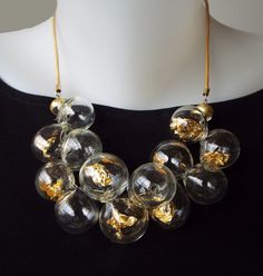 Unique and chic, This Glass beads bib necklace, for sure is a conversation starter. This Clear and Gold bubbles statement necklace combines transparent hollow glass beads, Filled with pieces of 22 karat gold leaf, in a cluster shape, connected to a Leather cord, and closes with a goldfilled clasp. The necklace has 2 inches (5 cm) chain to adjustable length. You can pair this unique necklace with these earrings: https://etsy.me/3Qg86lX This bold-blown airy jewelry is light and easy to wear, Perfe Luxury Adjustable Glass Necklace, Luxury Handmade Clear Necklace, Modern Gold Glass Necklace, Clear Glass Jewelry For Party, Modern Handmade Clear Necklaces, Unique Glass Necklace For Parties, Handmade Clear Jewelry For Party, Modern Glass Necklaces For Formal Occasions, Modern Glass Necklaces For Formal Events