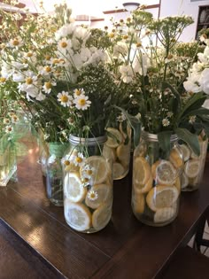 three mason jars filled with lemons and daisies sitting on a table next to flowers