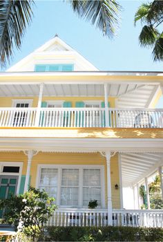 a yellow house with white balconies and green shutters on the second story