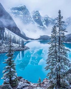 a lake surrounded by snow covered mountains and evergreen trees in the foreground, with blue water below