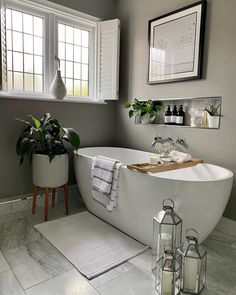 a white bath tub sitting in a bathroom next to a window and potted plants