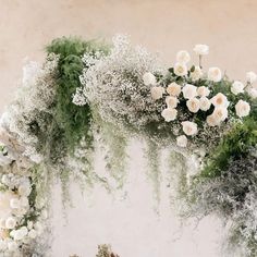 an arrangement of white flowers and greenery on a wall