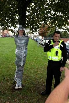 two police officers standing next to each other in the grass and one is dressed as an astronaut