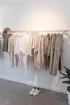 clothes are hanging on a rail in front of a potted plant and white wall