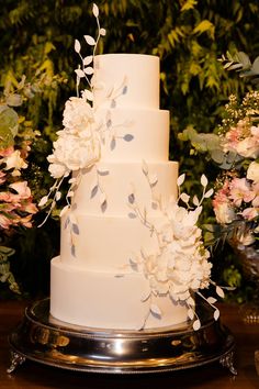 a wedding cake with white flowers and greenery in the background on a silver platter