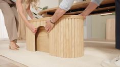 two people standing over a wooden table on top of a white carpeted floor next to each other