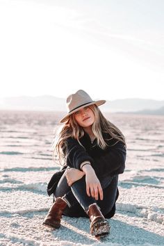 a woman sitting on the ground wearing a hat