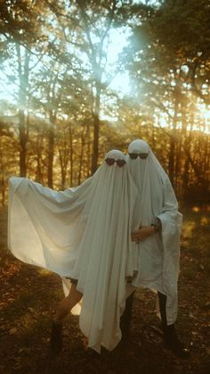 two people dressed in white are walking through the woods with long veils over their heads