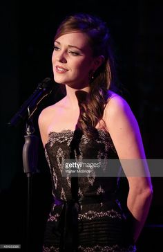 a woman standing at a microphone in front of a black background and wearing a strapless dress