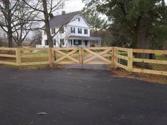 a wooden gate in front of a large white house with trees and grass around it