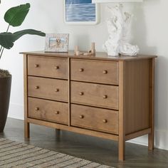 a wooden dresser sitting next to a potted plant in a white walled living room