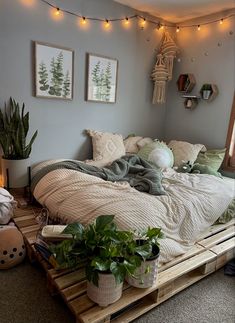 a bed made out of wooden pallets with plants on the bottom and hanging lights above it