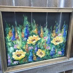 an oil painting of yellow and blue flowers in a wooden frame on a window sill