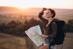 a woman with a backpack looking at a map in the distance while standing on top of a hill