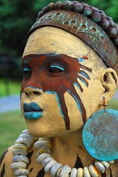 a woman with painted face and necklaces on her head is standing in the grass