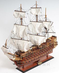 a wooden model ship with white sails is on display in front of a white background