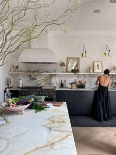 a woman in a black dress is standing at the kitchen counter